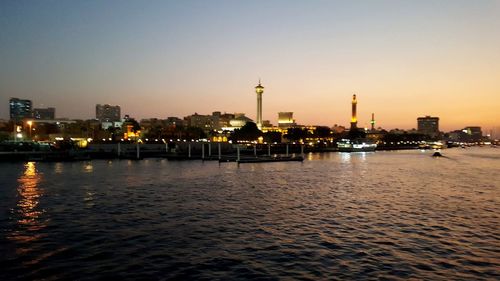 Illuminated city at waterfront during sunset