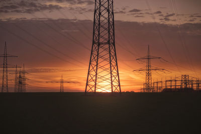 Silhouette electricity pylon against dramatic sky during sunset