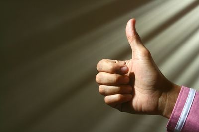 Close-up of hand gesturing thumbs up against rays