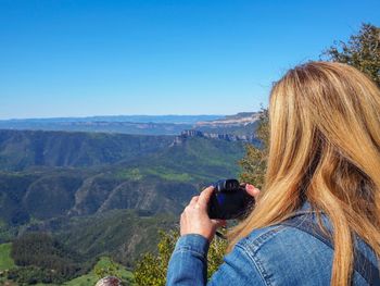 Man photographing on mountain against clear blue sky