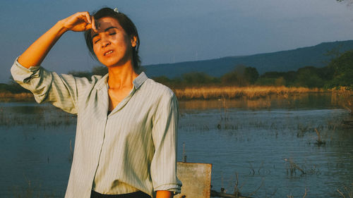 Portrait of young woman standing against lake