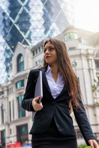 Young businesswoman walking against buildings in city