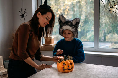 Mom and son in halloween costumes play together with jack-o-lantern spooky pumpkins lamp at home