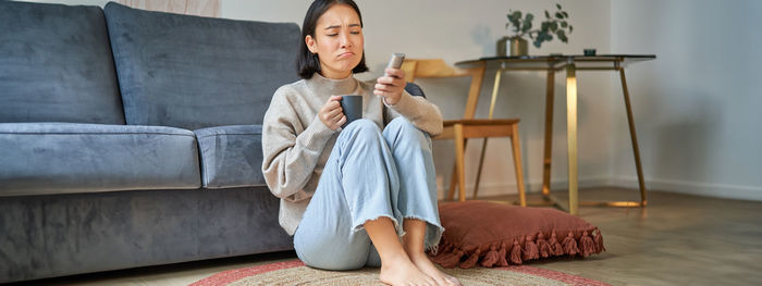 Young woman using mobile phone while sitting on sofa at home