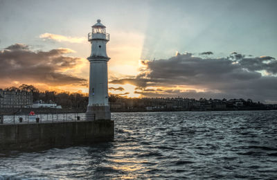 Lighthouse by sea against sky during sunset