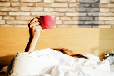 Woman holding coffee cup while sleeping on bed against wall