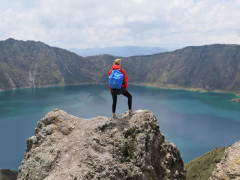 Man standing on rock by mountain against sky