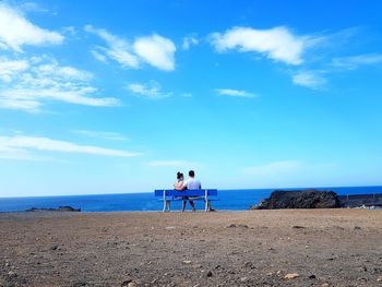 Rear view of couple standing at beach against blue sky