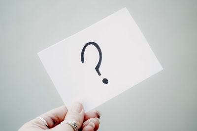 Cropped hand of woman holding paper against gray background