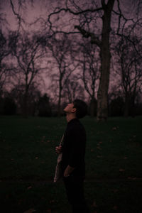 Side view of man standing by tree in forest