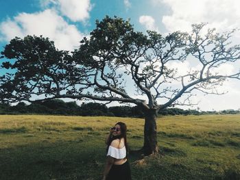 Portrait of woman standing on field against tree