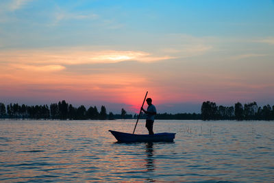 Man standing on boat in sea against sky during sunset