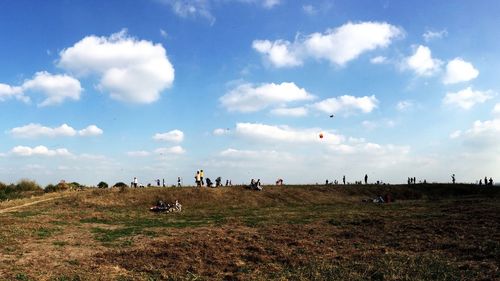 People on grassy field against cloudy sky