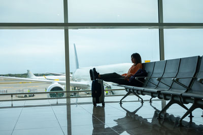 Woman with her feet on her suitcase, waiting for her flight at the airport.