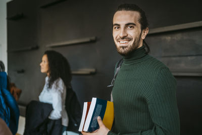 Portrait of smiling man holding books at community college