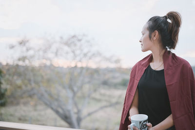 Young woman looking away while standing outdoors