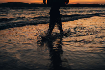 Low section of man standing at beach during sunset