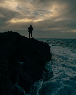 Silhouette man standing on rock by sea against sky during sunset