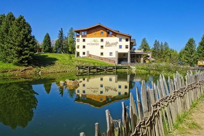 Reflection of building and trees in lake against blue sky