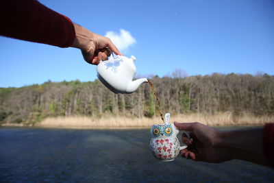 Midsection of man holding ice cream on field against sky