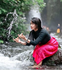 Young woman splashing water while sitting on rock