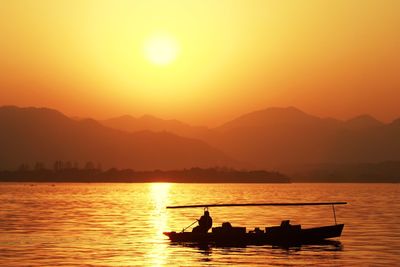 Silhouette boat moving on river against mountains during sunset