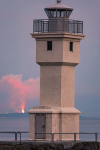Lighthouse by sea against sky during vulcano eruption
