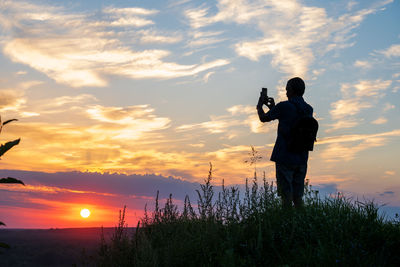 Rear view of man standing on field against sky during sunset