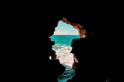 Silhouette people on rock formation in sea against sky