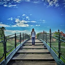 Full length of woman standing on footbridge against sky