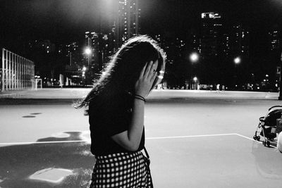 Rear view of woman standing on illuminated street at night