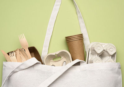 White textile bag and disposable tableware from brown craft paper on a green background. view from 