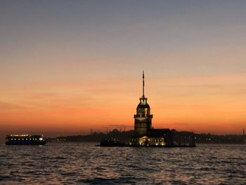 Illuminated building by sea against sky during sunset