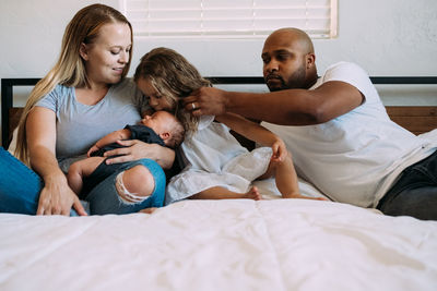 Multiracial family snuggling on bed with newborn baby