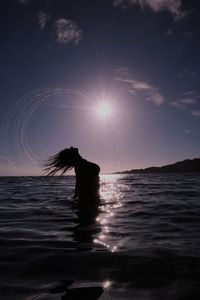 Silhouette of woman tossing wet hair while standing in sea against sky