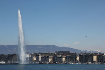 Waterfront scenic view of fountain in city against sky