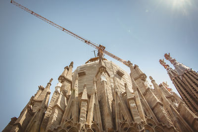 Low angle view of crane by building against sky