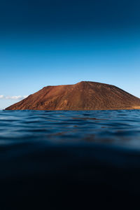 Red mountain of isla de lobos in fuerteventura at sunset from the sea