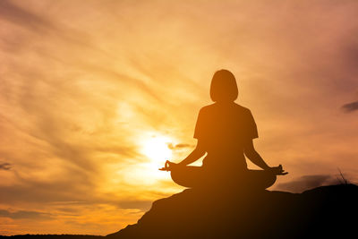 Woman meditating against sunset sky