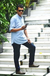 Full length of young man using mobile phone while standing on staircase