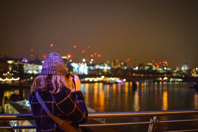 Rear view of man standing by river in city at night