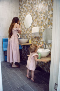 Mom and daughter standing in bathroom washing their hands and putting on lipstick.