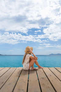 Rear view of woman sitting on pier over sea against sky