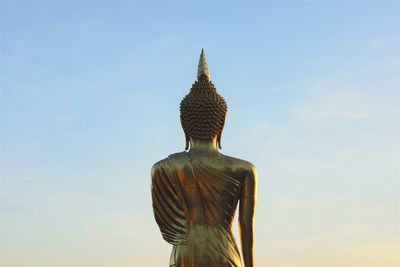 Low angle view of golden budda statue against sky