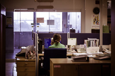 Rear view of woman using telephone while sitting at computer desk in office