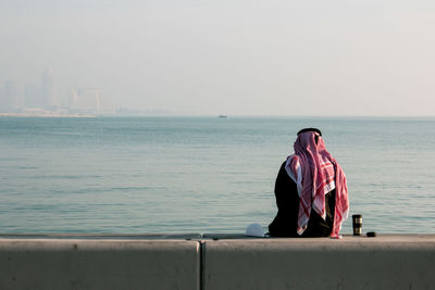 Rear view of man in traditional clothing while sitting by sea