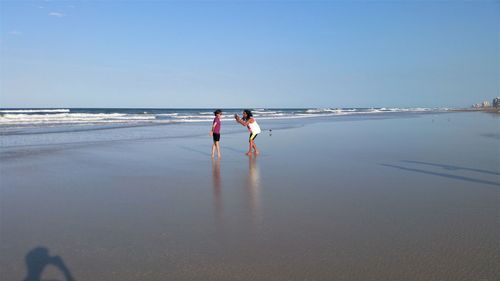 Man photographing woman at beach against sky