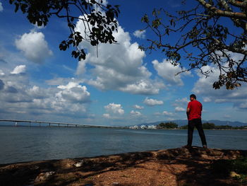 Rear view of man standing by sea against sky