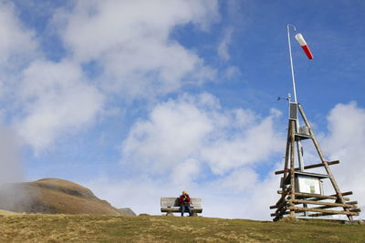 Person sitting on field by tower against sky