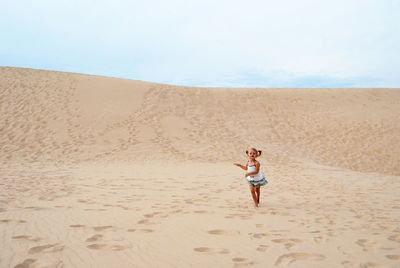 Full length of girl running on sand at beach against sky